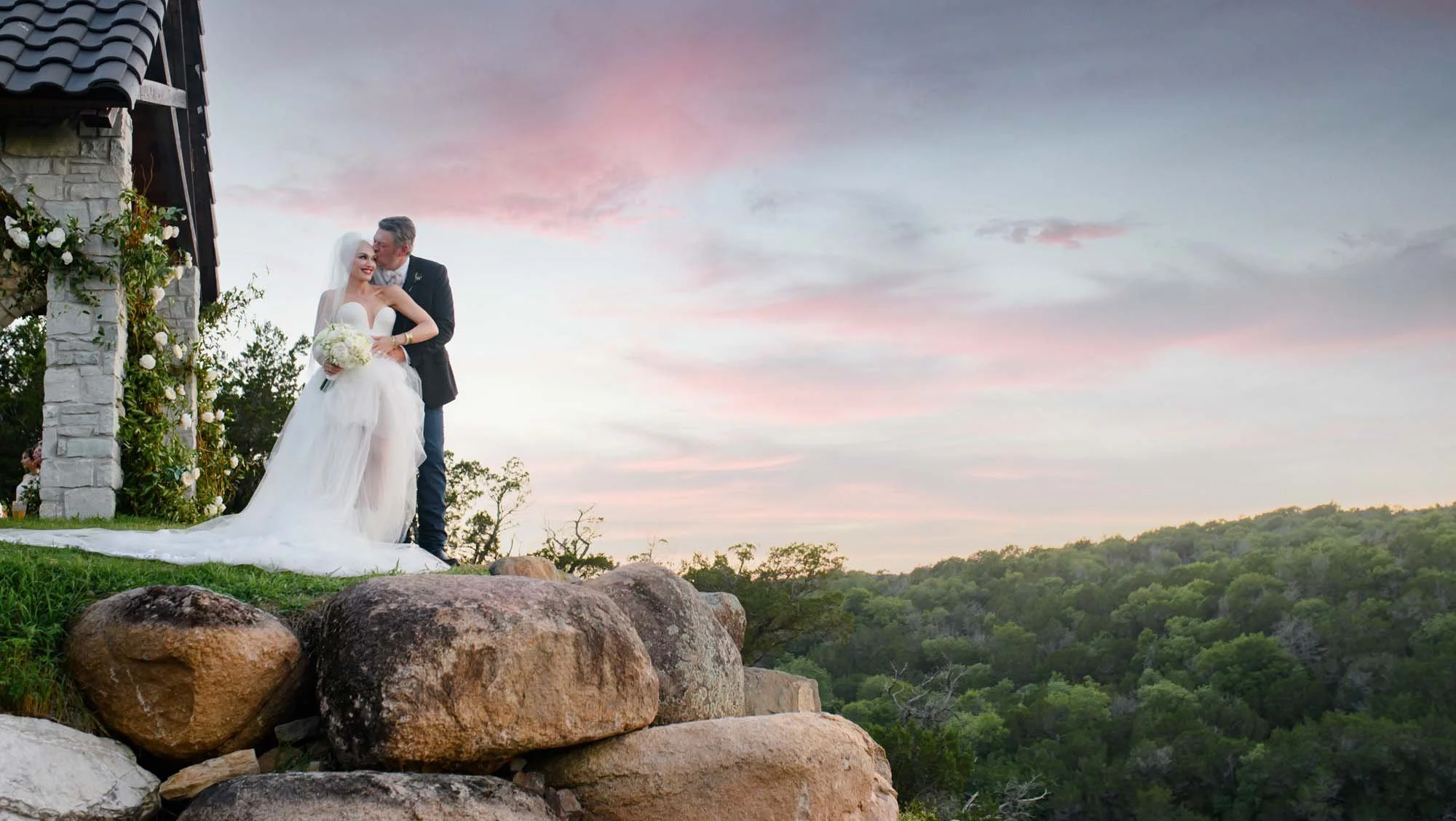 A wedding couple beneath a pink sunset beside a stone chapel